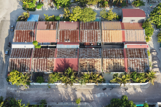 Aerial view of a row of houses with weathered rusty corrugated metal roofs surrounded by lush palm trees and tropical vegetation in Kudahuvadhoo Dhaalu Atoll Maldives.