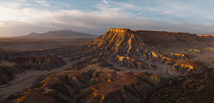 Aerial view of the rugged Caineville badlands illuminated by golden hour light showcasing dramatic eroded mesas and desert terrain in Caineville Utah United States.