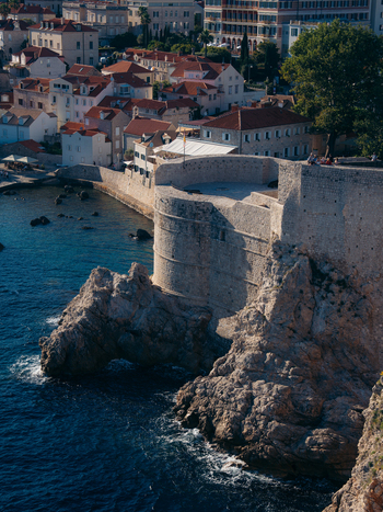 View of the historic stone walls and Bokar Fortress on rocky cliffs overlooking the blue Adriatic Sea and red roofed buildings in Dubrovnik Dubrovnik Neretva County Croatia. View of the historic stone walls and Bokar Fortress on rocky cliffs overlooking the blue Adriatic Sea and red roofed buildings in Dubrovnik Dubrovnik Neretva County Croatia.