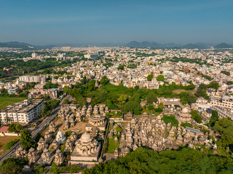 Aerial view of the historic Ahar Cenotaphs featuring stone domes and monuments surrounded by lush greenery with the urban cityscape in the background Udaipur Rajasthan India.