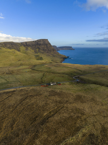 Aerial view of a camper parked near a small building on a winding road along the rugged cliffs and blue ocean Isle of Skye. Aerial view of a camper parked near a small building on a winding road along the rugged cliffs and blue ocean Isle of Skye.