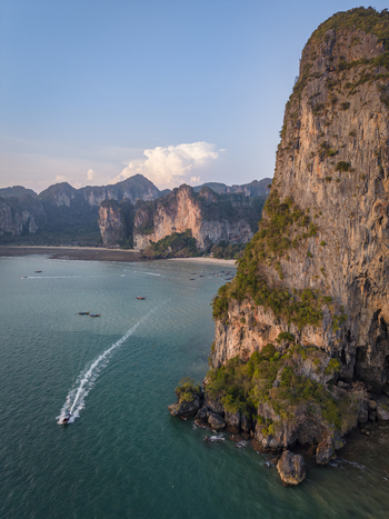 Aerial view of a boat cruising along the turquoise waters framed by towering limestone cliffs and lush greenery Krabi Thailand.
