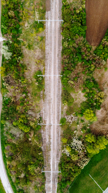 Aerial view of the converging railway lines cutting through vivid green trees and fields creating a stark contrast of industrial and natural elements Sremska Mitrovica Vojvodina Serbia. Aerial view of the converging railway lines cutting through vivid green trees and fields creating a stark contrast of industrial and natural elements Sremska Mitrovica Vojvodina Serbia.