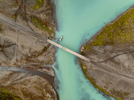 Aerial view of a bridge crossing a turquoise glacial river in the rugged volcanic landscape of Kerlingarfjoll with a vehicle driving across the bridge in Hrunamannahreppur Iceland. Aerial view of a bridge crossing a turquoise glacial river in the rugged volcanic landscape of Kerlingarfjoll with a vehicle driving across the bridge in Hrunamannahreppur Iceland.