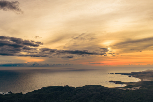 Aerial view of Punta Perula coastline at sunset with golden light over the Pacific Ocean and lush hills in Perula Jalisco Mexico.