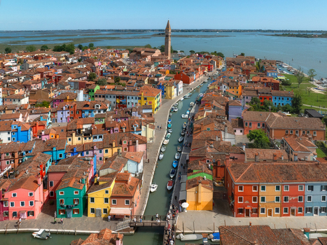 Aerial view of a vibrant canal lined with brightly painted houses under the warm sunlight crowned by the iconic leaning tower of Burano Venice Veneto Italy. Aerial view of a vibrant canal lined with brightly painted houses under the warm sunlight crowned by the iconic leaning tower of Burano Venice Veneto Italy.