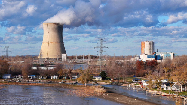 Aerial view of Davis Besse Nuclear Power Station with its cooling tower emitting steam power lines and industrial buildings near the waterfront in Oak Harbor Ohio United States.