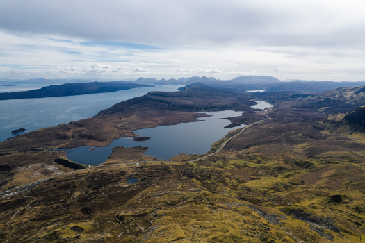 Aerial view of The Storr and the surrounding rugged landscape with a loch and coastal hills under a cloudy sky in Portree Scotland United Kingdom. Aerial view of The Storr and the surrounding rugged landscape with a loch and coastal hills under a cloudy sky in Portree Scotland United Kingdom.