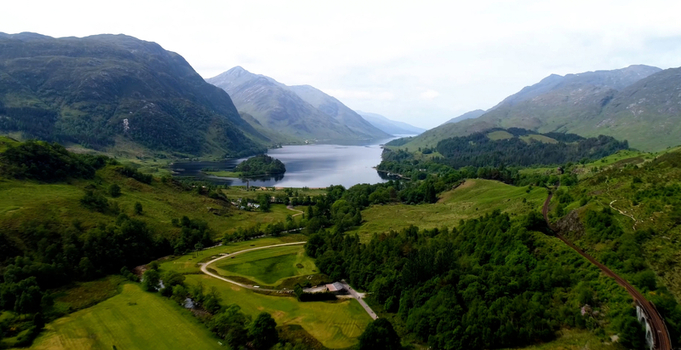 Aerial view of the iconic Glenfinnan Viaduct surrounded by lush green hills and the serene waters of Loch Shiel in Glenfinnan Scotland United Kingdom. Aerial view of the iconic Glenfinnan Viaduct surrounded by lush green hills and the serene waters of Loch Shiel in Glenfinnan Scotland United Kingdom.