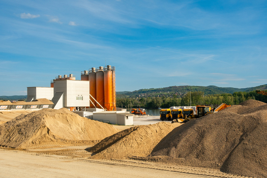 View of an industrial concrete plant with orange silos and large piles of gravel under a clear blue sky in Novi Sad Vojvodina Serbia. View of an industrial concrete plant with orange silos and large piles of gravel under a clear blue sky in Novi Sad Vojvodina Serbia.