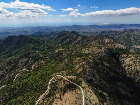 Aerial view of Kionia mountain peak with winding roads cutting through the lush green forests and rugged terrain under a bright blue sky in Lazanias Lefkosia Cyprus. Aerial view of Kionia mountain peak with winding roads cutting through the lush green forests and rugged terrain under a bright blue sky in Lazanias Lefkosia Cyprus.