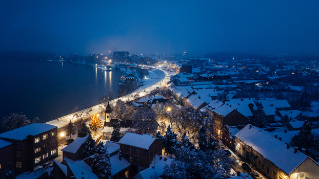 Aerial view of the snow covered town of Sremska Mitrovica at night with illuminated streets and a church along the riverbank in Sremska Mitrovica Vojvodina Serbia.