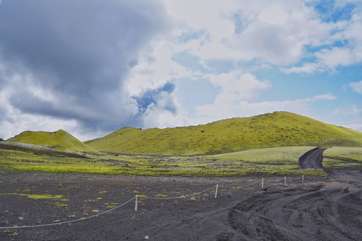 View of the moss covered volcanic landscape of Laki with black volcanic soil and a dirt road under a cloudy sky in Kirkjubaejarklaustur Skaftarhreppur Iceland. View of the moss covered volcanic landscape of Laki with black volcanic soil and a dirt road under a cloudy sky in Kirkjubaejarklaustur Skaftarhreppur Iceland.