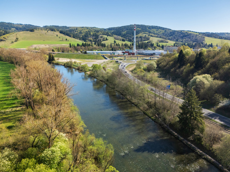 Aerial view of the Orava river and an industrial chimney surrounded by lush green hills in Nizna Zilina Region Slovakia.