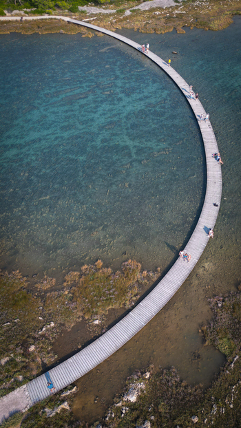 Aerial view of the curved wooden walkway of St. Anthony Channel near St. Nicholas Fortress over turquoise water with people walking along the path Sibenik Croatia.
