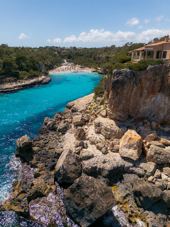 Aerial view of Cala Llombards beach and turquoise bay surrounded by rocky cliffs and people on the sand in Cala Llombards Illes Balears Spain. Aerial view of Cala Llombards beach and turquoise bay surrounded by rocky cliffs and people on the sand in Cala Llombards Illes Balears Spain.