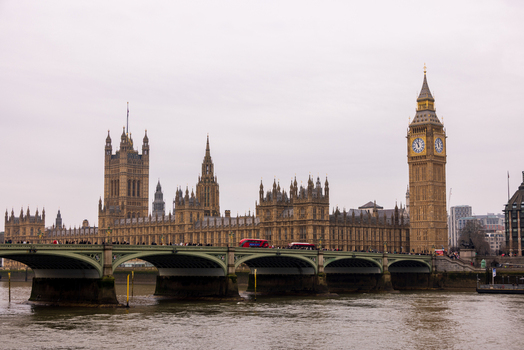 London United Kingdom 12 May 2025 View of the Palace of Westminster and Big Ben across the River Thames with Westminster Bridge and a red bus under an overcast sky.