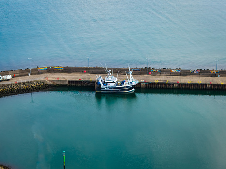 Aerial view of a fishing boat moored in Bangor Harbour with stone pier walls and calm turquoise water in Bangor Northern Ireland United Kingdom.