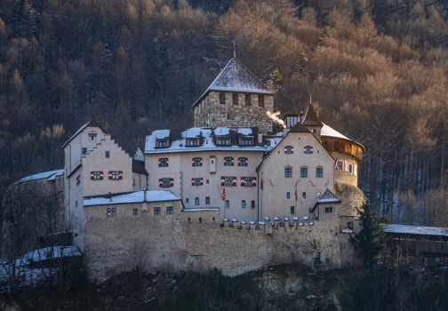 View of Vaduz Castle with its medieval stone walls and snow covered rooftops nestled against a forested hillside during the golden hour in Vaduz Vaduz Liechtenstein.
