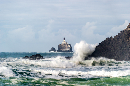 View of Tillamook Rock Lighthouse perched on a rocky island surrounded by crashing ocean waves and a cloudy sky in Cannon Beach Oregon United States. View of Tillamook Rock Lighthouse perched on a rocky island surrounded by crashing ocean waves and a cloudy sky in Cannon Beach Oregon United States.