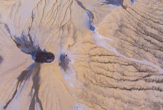 Aerial view of mud volcanoes at Vulcanii Noroiosi Paclele Mari showing intricate patterns of dried mud small craters and a person standing near a vent in Paclele Buzau County Romania.