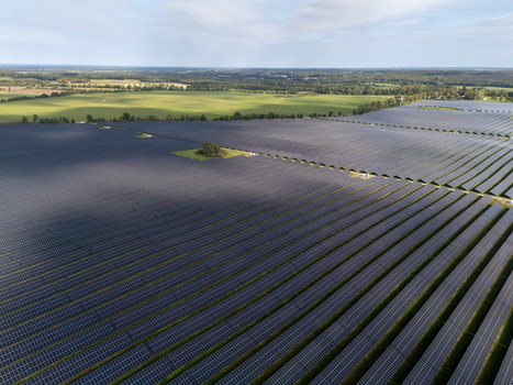 Aerial view of a vast solar farm with rows of photovoltaic panels stretching across the landscape under a partly cloudy sky in Poland.