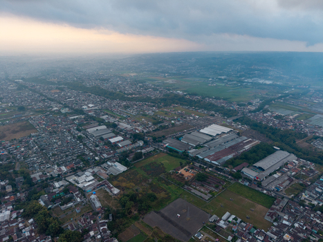 Aerial view of the urban landscape featuring dense residential areas industrial warehouses and surrounding green fields in Malang East Java Indonesia.
