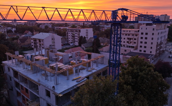 Aerial view of a construction site with a tall blue crane towering over a building under development during a vibrant sunset in Pancevo Vojvodina Serbia.