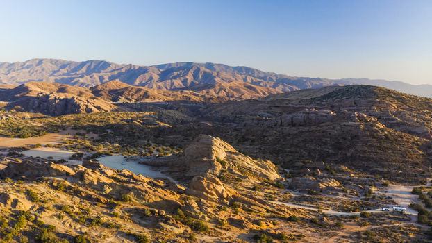 Aerial view of rugged desert rock formations and a small pond surrounded by arid hills under a clear sky in the United States. Aerial view of rugged desert rock formations and a small pond surrounded by arid hills under a clear sky in the United States.