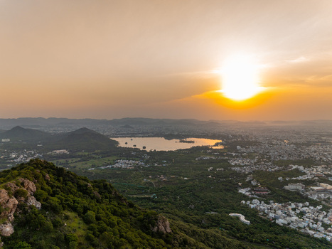 Aerial view of the city of Udaipur surrounded by lush green hills and lakes during a golden sunset in Udaipur Rajasthan India.