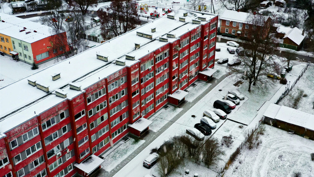 Aerial view of a red apartment building surrounded by snow covered grounds parking lot with cars and a playground in Latvija. Aerial view of a red apartment building surrounded by snow covered grounds parking lot with cars and a playground in Latvija.