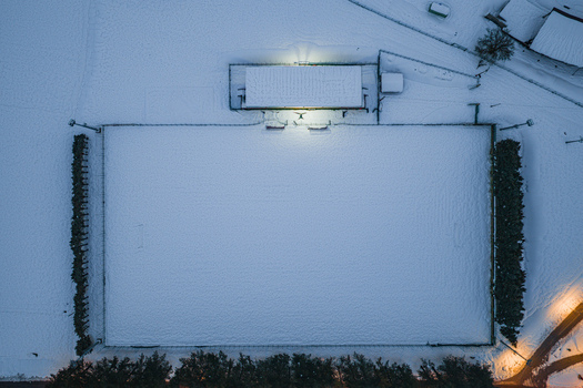 Aerial view of a snow covered soccer field illuminated by bright floodlights at night in Rivisondoli Abruzzo Italy.