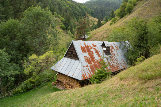 View of a rustic cabin with a rusty metal roof nestles against a verdant hillside surrounded by trees Prasnica Banska Bystrica Region Slovakia. View of a rustic cabin with a rusty metal roof nestles against a verdant hillside surrounded by trees Prasnica Banska Bystrica Region Slovakia.