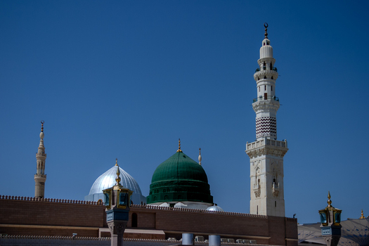 View of Al Masjid e Nabawi with its iconic green dome and minarets against a clear blue sky in Madinah Al Madinah Province Saudi Arabia.