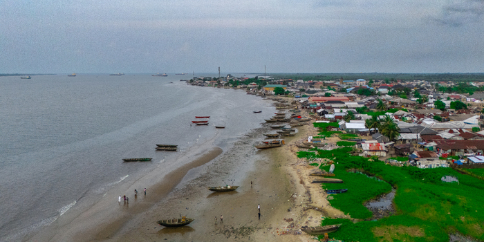 Aerial view of Bonny Island featuring wooden boats on the sandy beach residential buildings and ships in the distance in Bonny Town Rivers Nigeria. Aerial view of Bonny Island featuring wooden boats on the sandy beach residential buildings and ships in the distance in Bonny Town Rivers Nigeria.