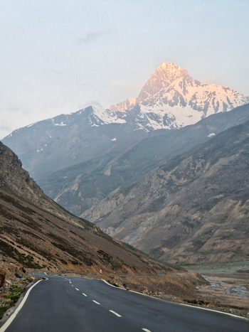 View of a winding road leading towards the snow capped Himalayan peaks Malana Himachal Pradesh India.