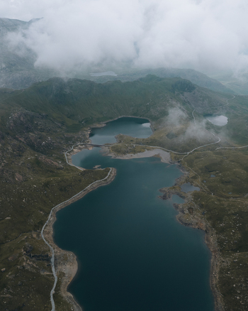 Aerial view of the glacial lakes surrounding Snowdon with rugged mountain slopes winding paths and low hanging clouds in Caernarfon Wales United Kingdom.