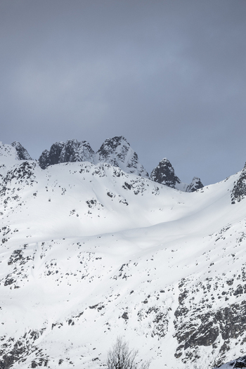 View of snow covered jagged mountain peaks under a cloudy winter sky in Ersfjord Troms Norway. View of snow covered jagged mountain peaks under a cloudy winter sky in Ersfjord Troms Norway.