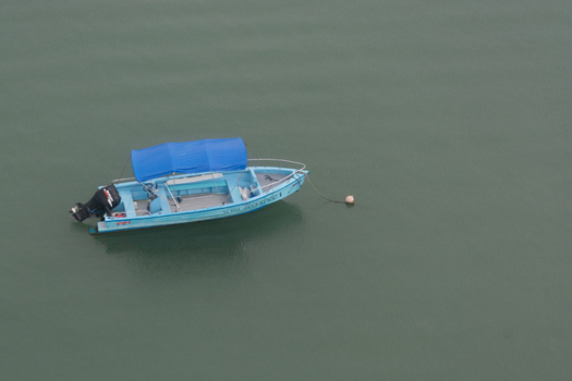 View of a small light blue motorboat with a blue canopy floating on calm dark water in Costa Rica. View of a small light blue motorboat with a blue canopy floating on calm dark water in Costa Rica.