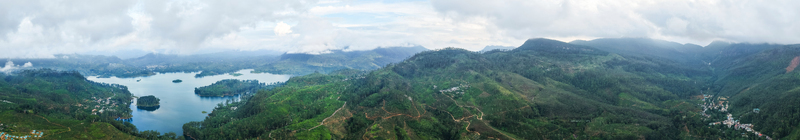 Aerial view of the panoramic Moussakelle Reservoir surrounded by lush green hills and tea plantations under a cloudy sky in Nallathanniya Central Province Sri Lanka.