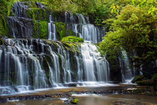 View of Purakaunui Falls cascading over moss covered rocks in a lush forest setting in Purakaunui Otago Region New Zealand.