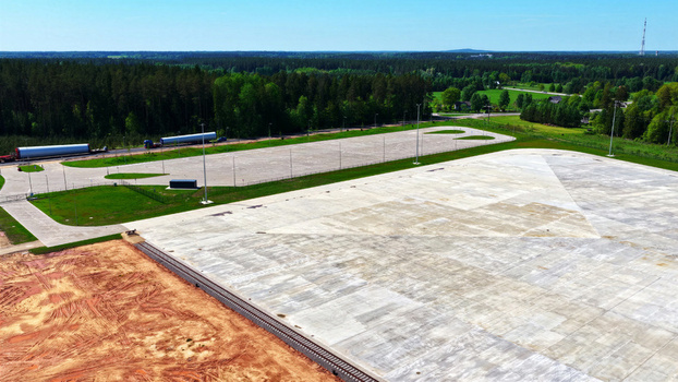 Aerial view of a large concrete industrial staging area with wind turbine blades on a truck surrounded by forest and cleared land in Latvia. Aerial view of a large concrete industrial staging area with wind turbine blades on a truck surrounded by forest and cleared land in Latvia.