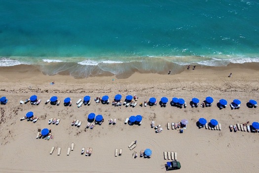 Aerial view of Singer Island beach with rows of blue umbrellas and people relaxing by the turquoise ocean waves Riviera Beach Florida United States. Aerial view of Singer Island beach with rows of blue umbrellas and people relaxing by the turquoise ocean waves Riviera Beach Florida United States.