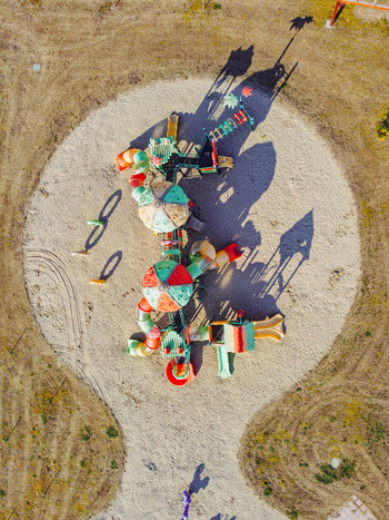 Aerial view of a colorful children s playground with slides and climbing frames on a circular sand pit surrounded by dry grass in Turin Piedmont Italy. Aerial view of a colorful children s playground with slides and climbing frames on a circular sand pit surrounded by dry grass in Turin Piedmont Italy.