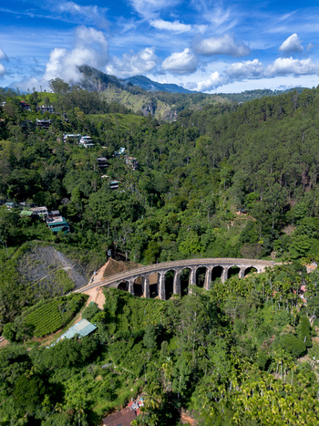 Aerial view of the iconic Nine Arch Bridge surrounded by lush green tea plantations dense forest and rolling hills under a bright blue sky in Demodara Uva Province Sri Lanka. Aerial view of the iconic Nine Arch Bridge surrounded by lush green tea plantations dense forest and rolling hills under a bright blue sky in Demodara Uva Province Sri Lanka.