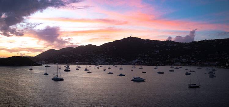 Aerial view of Charlotte Amalie bay at sunset with numerous boats anchored in calm water against rolling hills and a vibrant sky in Charlotte Amalie St. Thomas U.S. Virgin Islands.