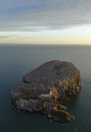 Aerial view of Bass Rock Lighthouse on a steep volcanic island surrounded by the calm sea under a soft morning sky North Berwick Scotland United Kingdom. Aerial view of Bass Rock Lighthouse on a steep volcanic island surrounded by the calm sea under a soft morning sky North Berwick Scotland United Kingdom.