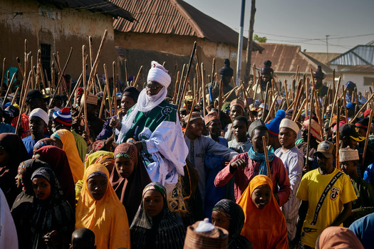 Zaria City Nigeria 22 March 2026 View of a vibrant crowd of people some holding tall wooden staffs surrounding a dignified figure in striking white and green robes under the bright sun. Zaria City Nigeria 22 March 2026 View of a vibrant crowd of people some holding tall wooden staffs surrounding a dignified figure in striking white and green robes under the bright sun.