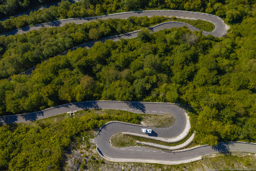 Aerial view of a winding mountain road snaking through a dense green forest with a vehicle driving along the curves Spodnja Sorica Skofja Loka Slovenia.