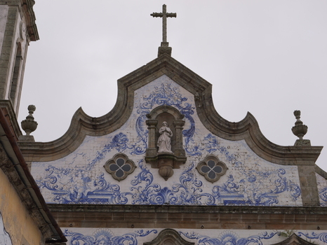 View of the facade of Church of Santa Maria Maior with blue and white azulejo tiles a central statue and a stone cross in Covilha Castelo Branco Portugal. View of the facade of Church of Santa Maria Maior with blue and white azulejo tiles a central statue and a stone cross in Covilha Castelo Branco Portugal.